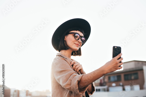 Cute and pretty fashion trendy and hipster millennial woman or girl makes selfie on smartphone camera to share on internet social media channels, self absorbed new generation of young people photo
