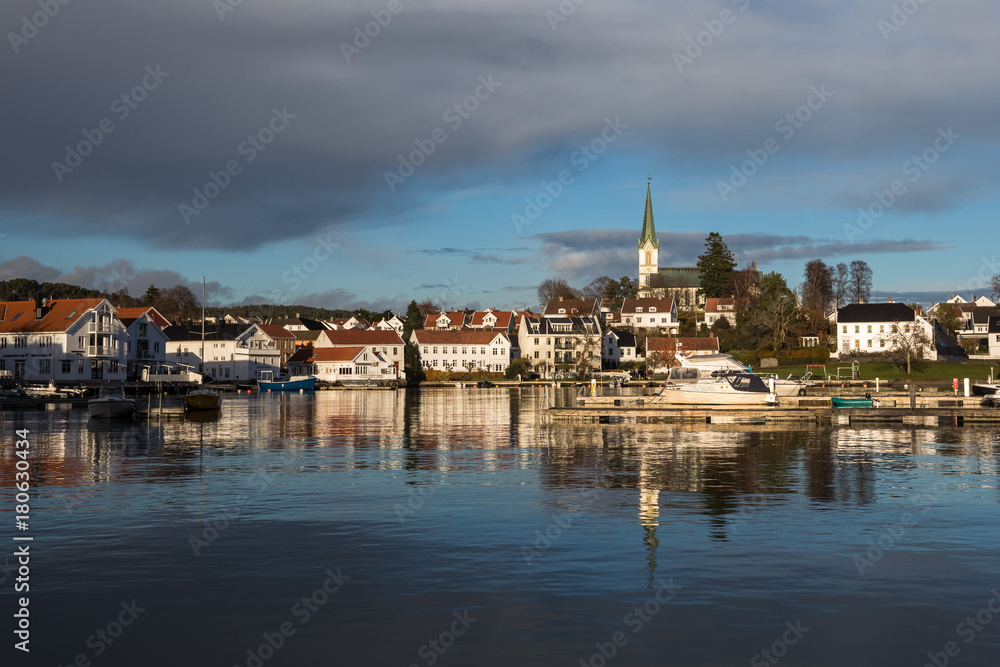 Lillesand, Norway - November 10, 2017: Lillesand City seen from the harbor. Blue sky and clouds, reflections of city in the ocean.