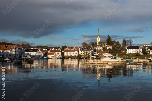 Lillesand, Norway - November 10, 2017: Lillesand City seen from the harbor. Blue sky and clouds, reflections of city in the ocean.