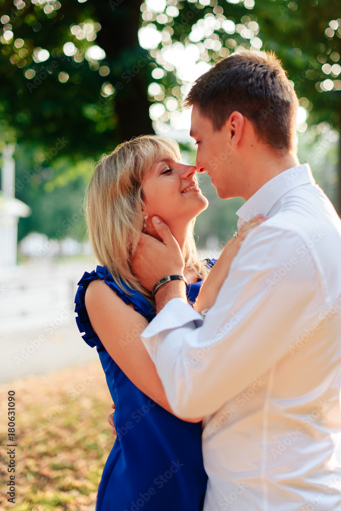 beautiful couple in love with a woman walking in a park on a bench kissing at sunset and loving each other, a blue dress and a white shirt with jeans beautiful couple in love with a woman walking in a park on a bench kissing at sunset and loving each other, a blue dress and a white shirt with jeans