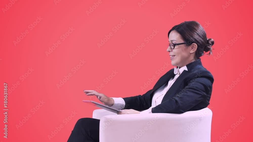 Business woman with glasses sitting in the Studio in a business suit and gives interviews. Writes information on the screen and smiles. Red background. Business woman with glasses sitting in the Studio in a business suit and gives interviews. Writes information on the screen and smiles. Red background.