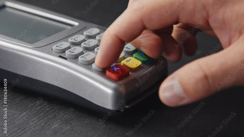 Man's hand pushing the buttonon pos terminal standing on black wooden desk.