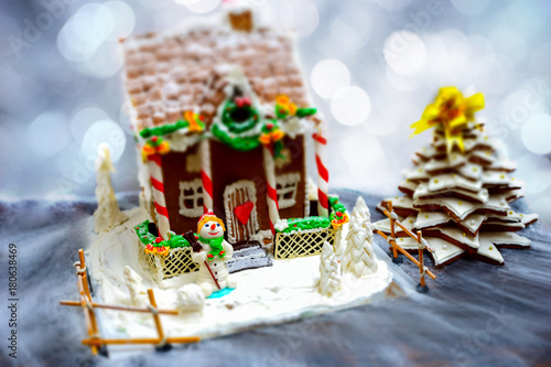 Homemade gingerbread house, gingerbread Christmas tree and a sugar mastic snowman on background of defocused silver lights © kolotype