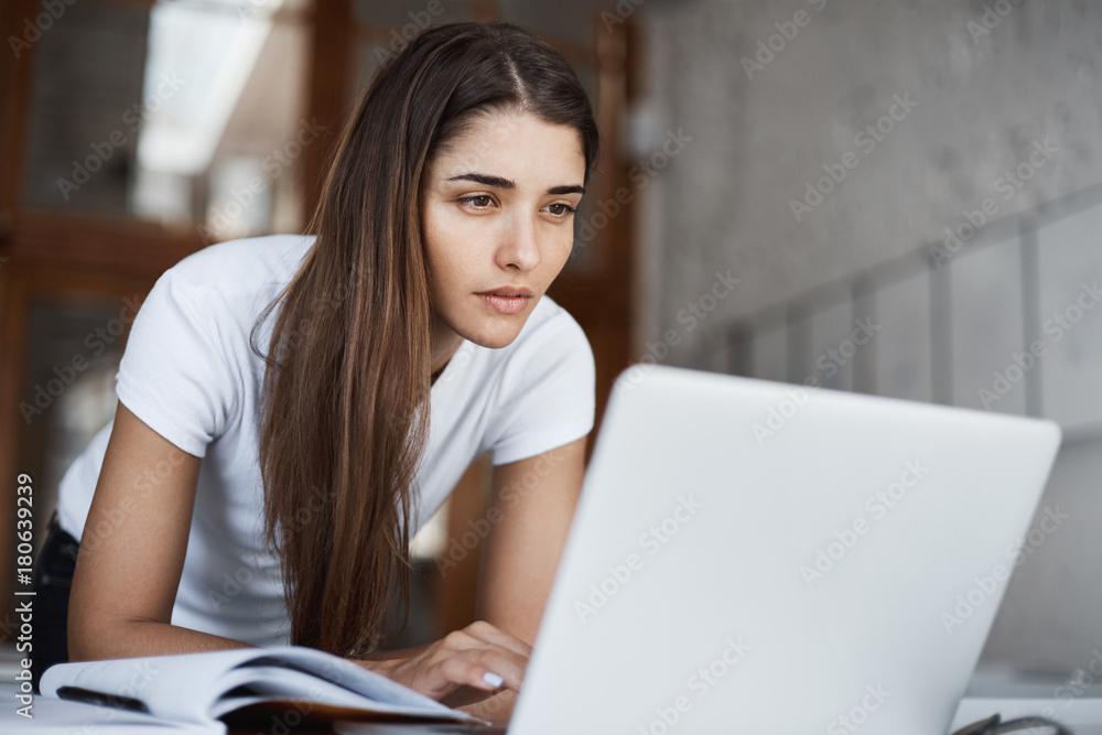 Fototapeta premium Young beautiful student browsing internet on a laptop computer searching for new information on university library.