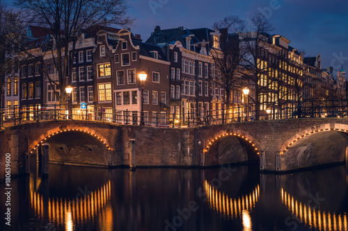 Photography Old historic houses, canal, and a bridge during twilight blue hour, Amsterdam, N