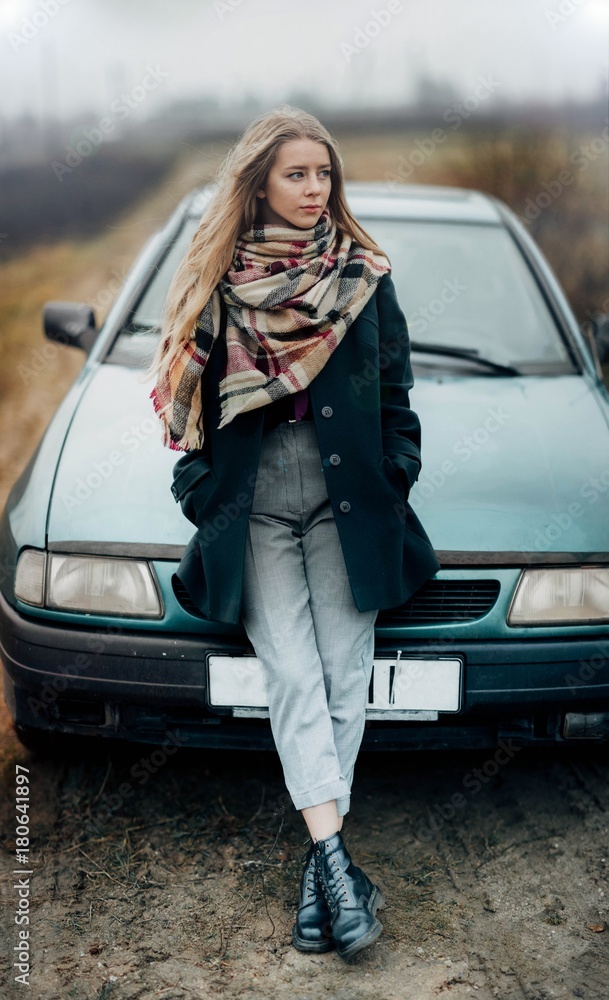 the female driver stands by the car in the cold season. Blonde on the hood