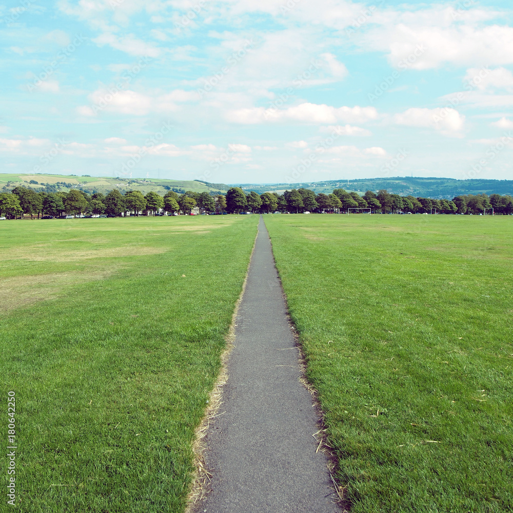 long straight footpath stratching to the distance in a park with grass lawn and trees in the background in halifax yorkshire