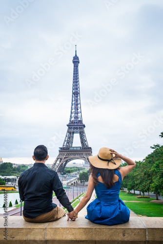 Young couple of tourists sitting in front of Eiffel tower in Paris, vertical view © evafonina