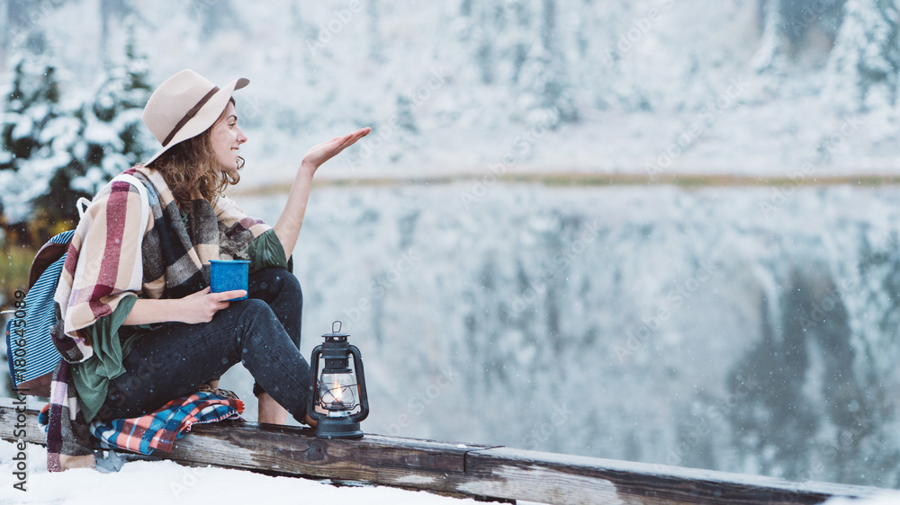 Smiling pretty woman with hot drink catching first snow and spending vacations among stunning winter landscape. Traveling in mountains wilderness. Wanderlust and boho style Smiling pretty woman with hot drink catching first snow and spending vacations among stunning winter landscape. Traveling in mountains wilderness. Wanderlust and boho style