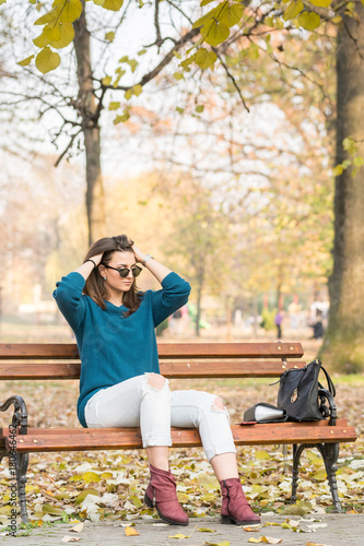 Young beautiful teenage girl sitting on the park bench and holding her hair