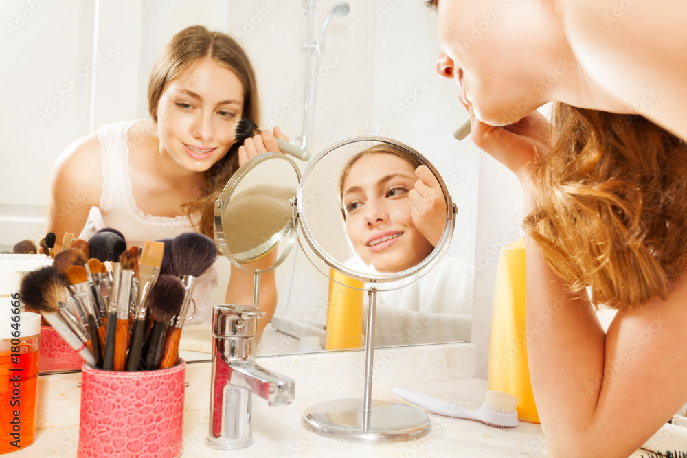 Young woman apply makeup, seen in bathroom mirror