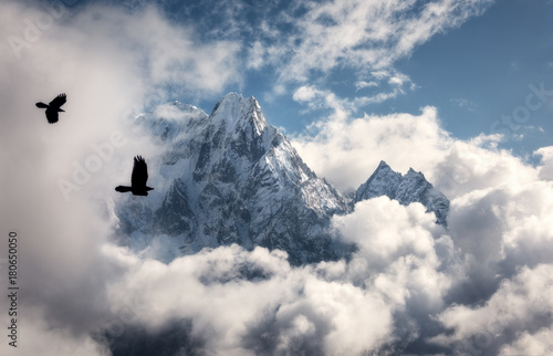 Two flying birds against majestical Manaslu mountain with snowy peak in clouds in sunny bright day in Nepal. Landscape with beautiful high rocks and blue cloudy sky. Nature background. Fairy scene
