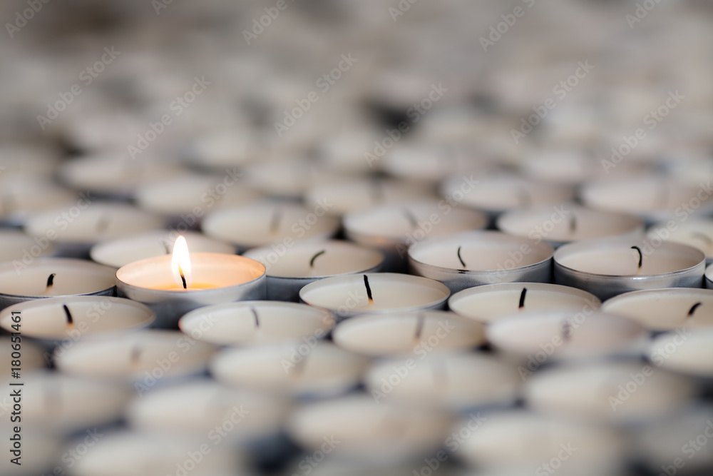 Naklejka premium Shining light from a solitary burning candle flame. Selective focus on one tealight among many.