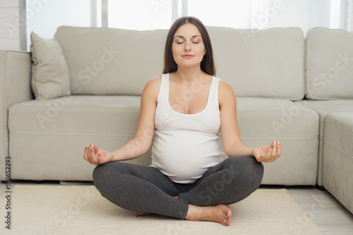 Pregnant sport. A pregnant woman sits on a light floor at home. She does yoga exercises