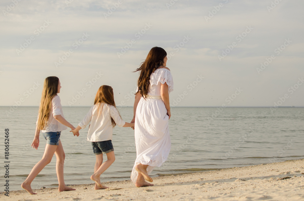 Woman with daughters is walking along a paradise beach. Mom and sisters are traveling on the island