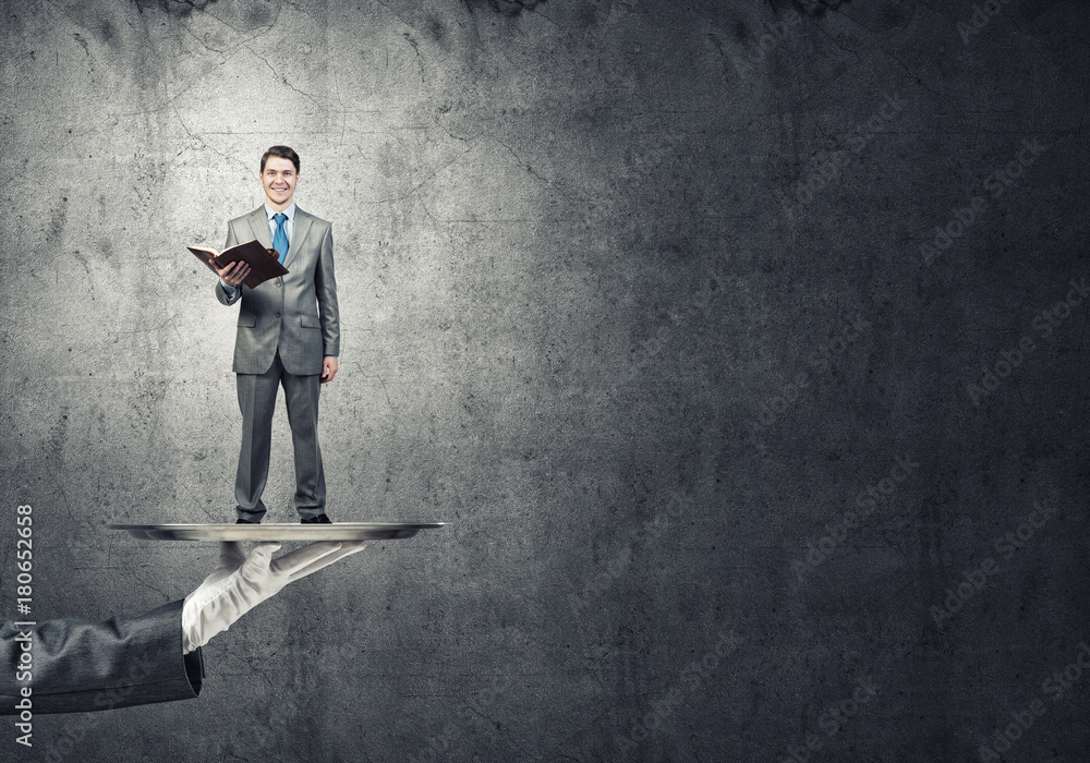 Businessman on metal tray with red book in hands against concrete background Businessman on metal tray with red book in hands against concrete background