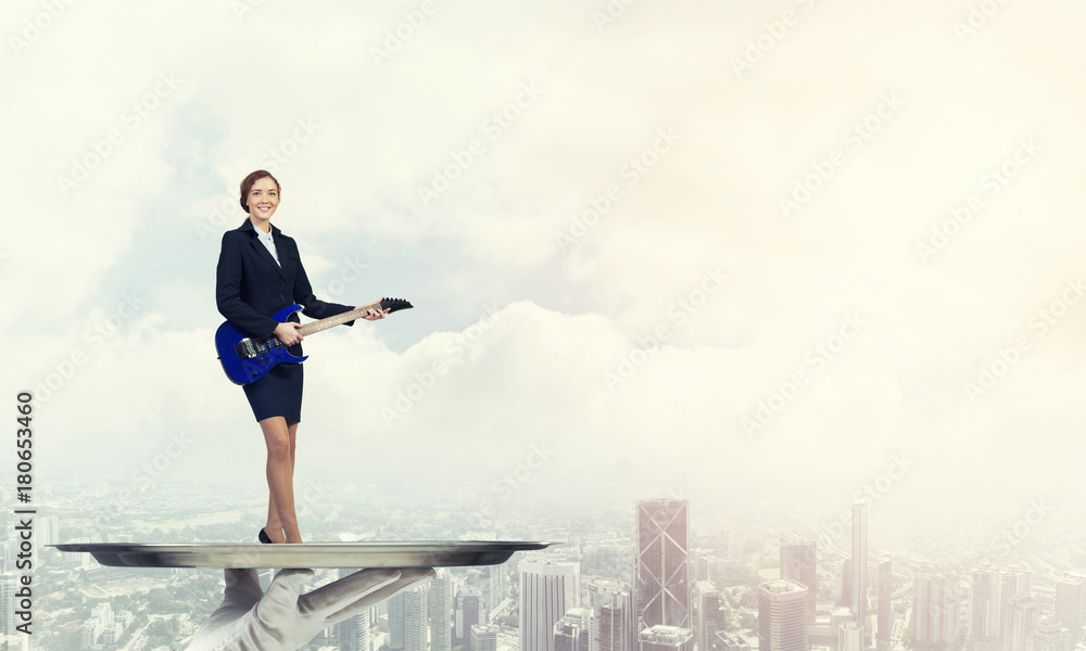 Attractive businesswoman on metal tray playing electric guitar against cityscape background Attractive businesswoman on metal tray playing electric guitar against cityscape background
