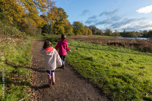 Two young girls enjoying walk in Autumn on a beautiful sunny day at the park, Abbey Fields, Kenilworth, Warwickshire, England, November 2017.