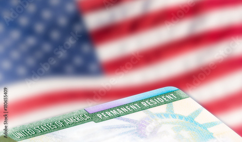 United States of America permanent resident card, green card, with US flag in the background. Legal immigration concept.
