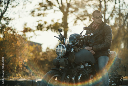 Motorcyclist sits on an old cafe-racer motorcycle, autumn background