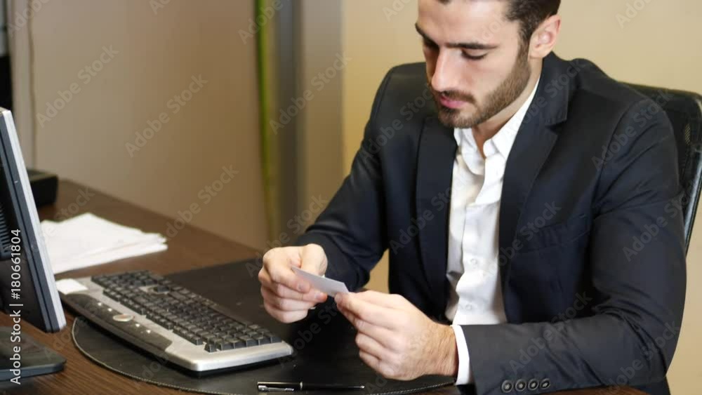 Handsome businessman sitting at table in his office and taking visiting or business card from another man. Handsome businessman sitting at table in his office and taking visiting or business card from another man.
