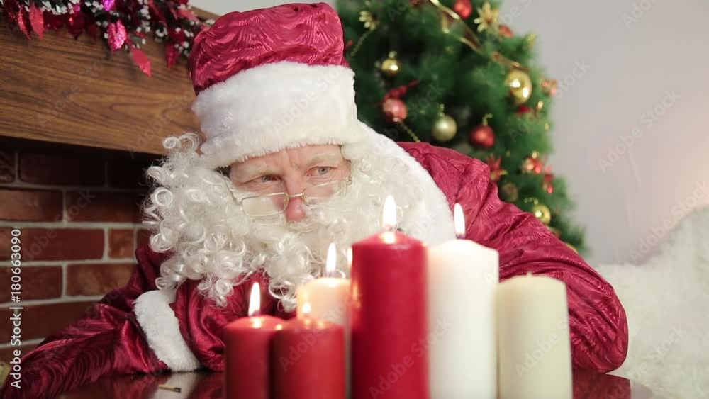 Santa Claus blows out the candles. Santa Claus wants to put out the red and white New Year candles, blowing air on them. Santa Claus blows out the candles. Santa Claus wants to put out the red and white New Year candles, blowing air on them.