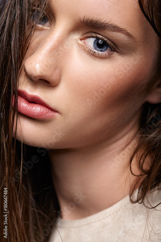 Beauty portrait of young woman. Brunette girl with bright blue eyes and day female makeup on gray background