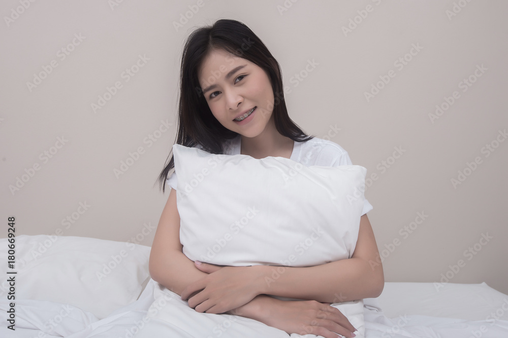 Smiling young woman hugging with pillow sitting on bed at home in bedroom. Smiling young woman hugging with pillow sitting on bed at home in bedroom.