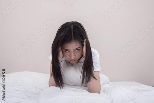 Depressed young woman sitting on bed.
