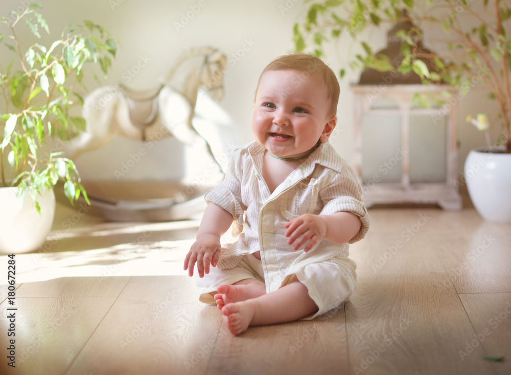 a small child in a shirt sits in a spacious light room with toys in the background