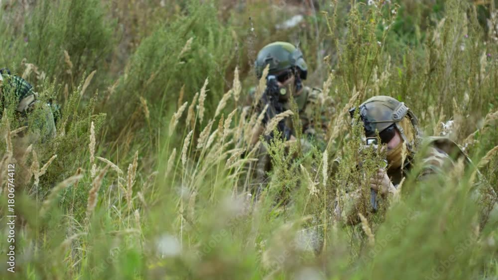 Tracking shot of soldiers in camouflage sitting in the grass and aiming shotguns at camera Tracking shot of soldiers in camouflage sitting in the grass and aiming shotguns at camera