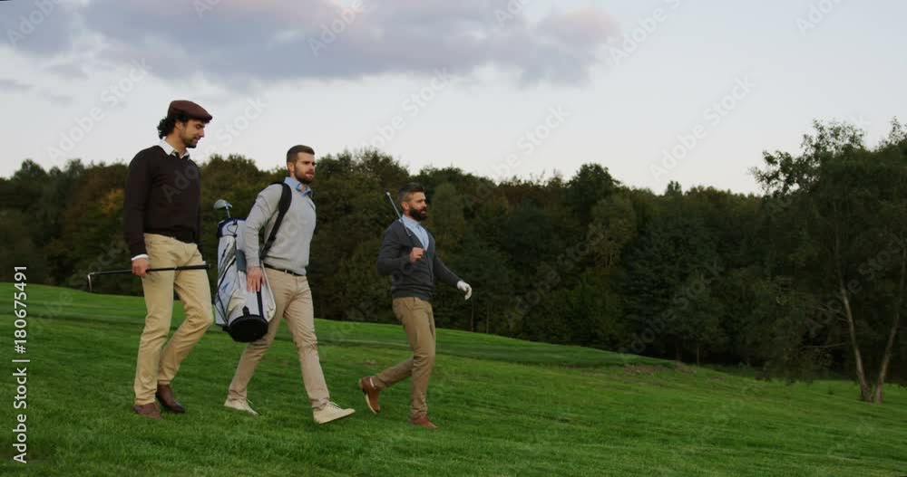 Handsome male friends walking with their clubs on the golf pitch to play a game, talking and laughing. Handsome male friends walking with their clubs on the golf pitch to play a game, talking and laughing.