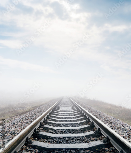 railroad in meadow with fog and clouds over it
