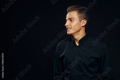 man in black shirt on black background looks away and smiles