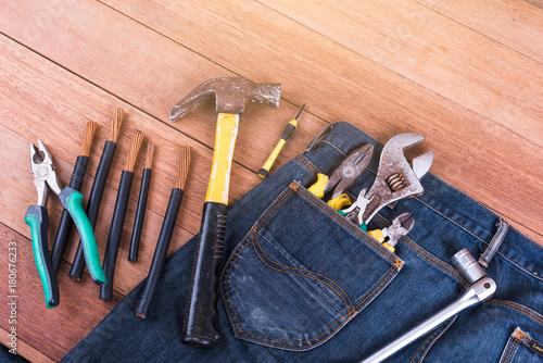 Several tools in a denim workers pocket on wood planks