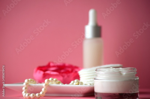A jar of luxury beauty face cream and serum bottle with pearls on pink color background with copy space. Styled feminine lifestyle image. 