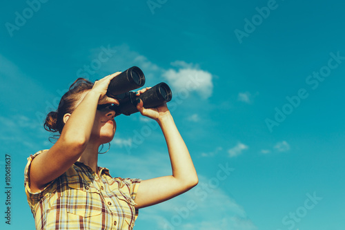 Beautiful Young Girl Looking Through Binoculars On Blue Sky Background. Travel Holidays Journey Concept