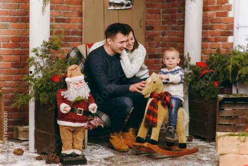 Young happy parents with a cute little child boy on rocking horse, dressed in sweater in decorated New Year room with Santa at home. Christmas good mood. Lifestyle, family and holiday 2018 concept