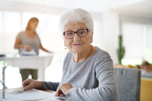 Portrait of old woman reading newspaper while homehelp irons