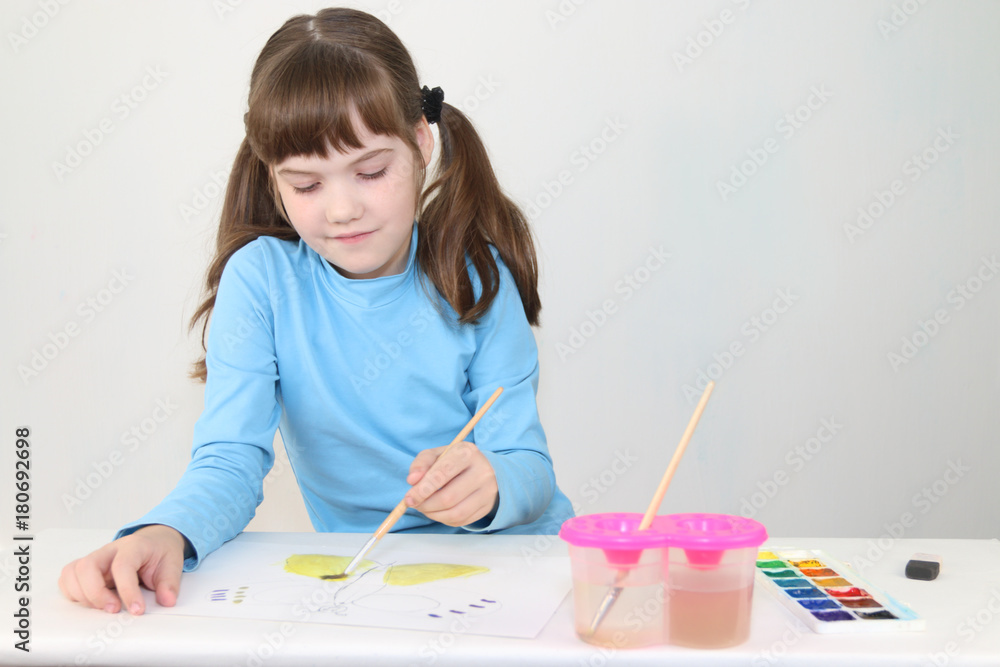 Smiling girl in blue watercolor paints butterfly on table in white room Smiling girl in blue watercolor paints butterfly on table in white room