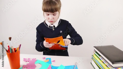 School girl cuts out with scissors from colored paper