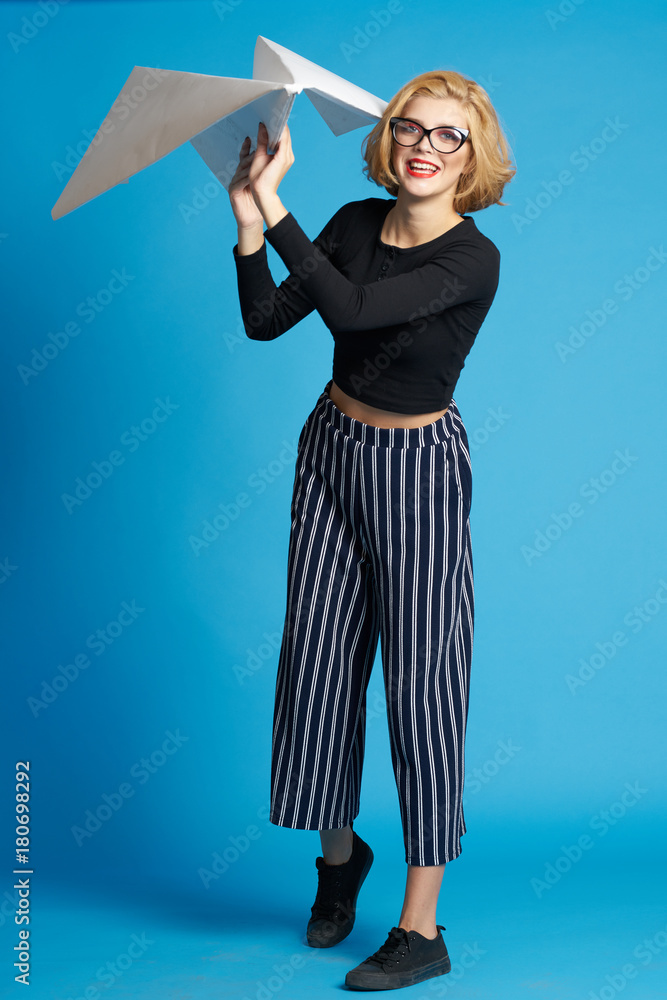 Fototapeta premium woman in glasses with a big paper airplane on a blue background smiling