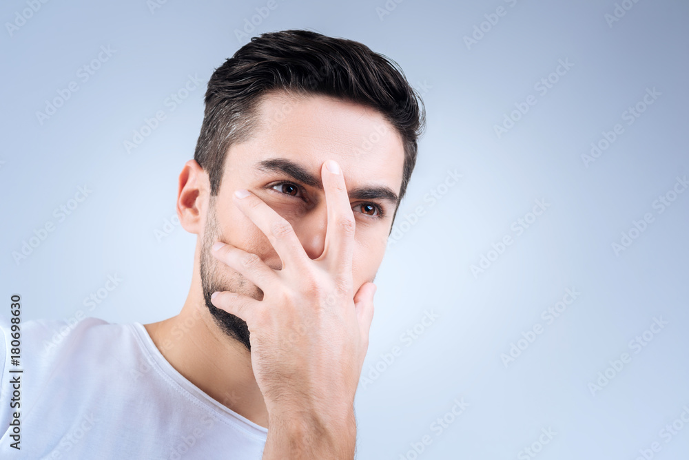 Hiding face. Mysterious serious young person looking weird while standing and closing half of his face with a hand Hiding face. Mysterious serious young person looking weird while standing and closing half of his face with a hand