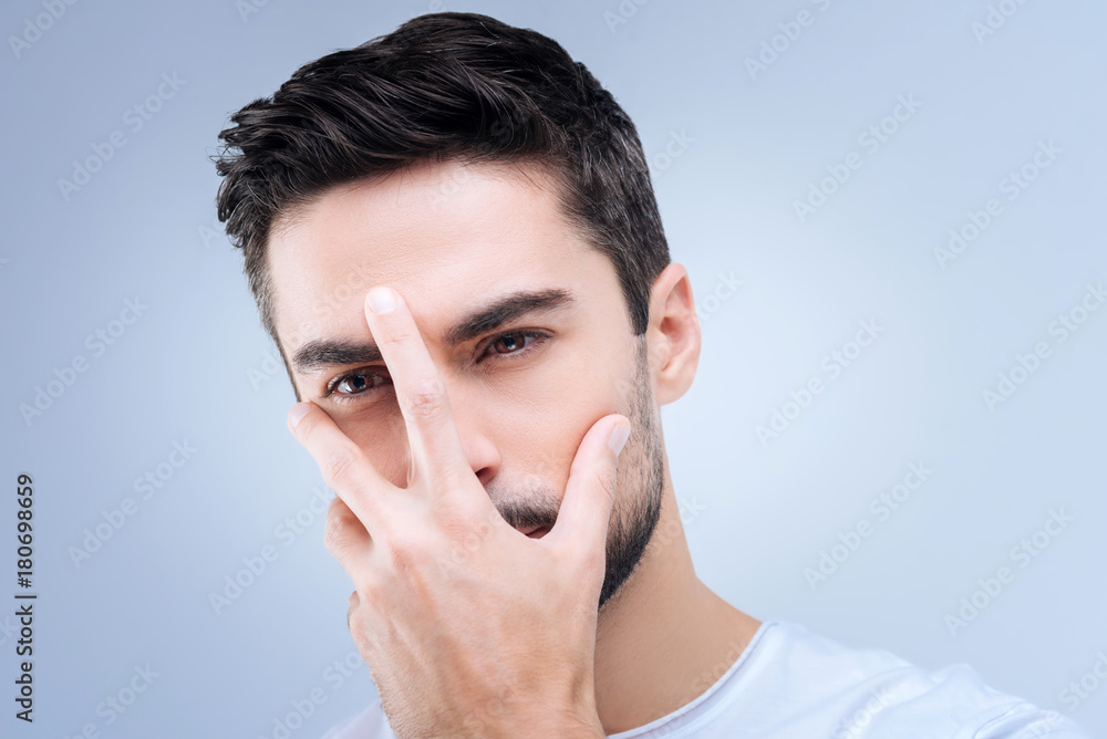 Hidden emotions. Serious unhappy young person standing with a hand on his face while looking gloomy and rejecting to show his face and express his feelings Hidden emotions. Serious unhappy young person standing with a hand on his face while looking gloomy and rejecting to show his face and express his feelings