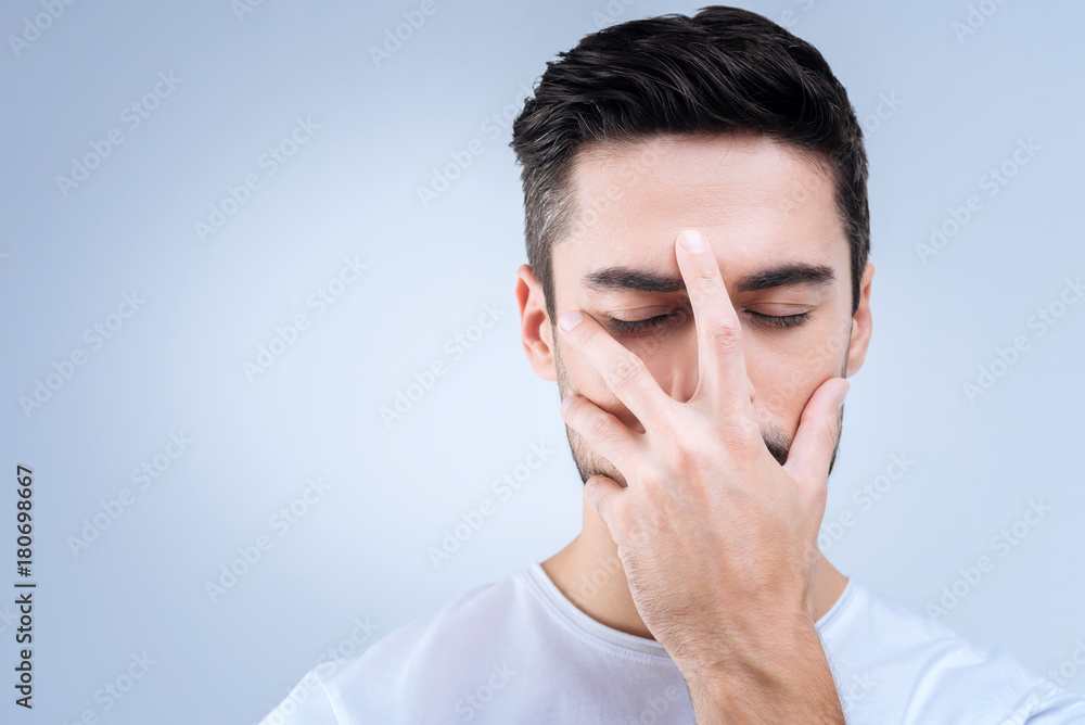 Painful memories. Young serious unhappy man standing with his eyes closed and hiding his face while remembering bad events from his past Painful memories. Young serious unhappy man standing with his eyes closed and hiding his face while remembering bad events from his past