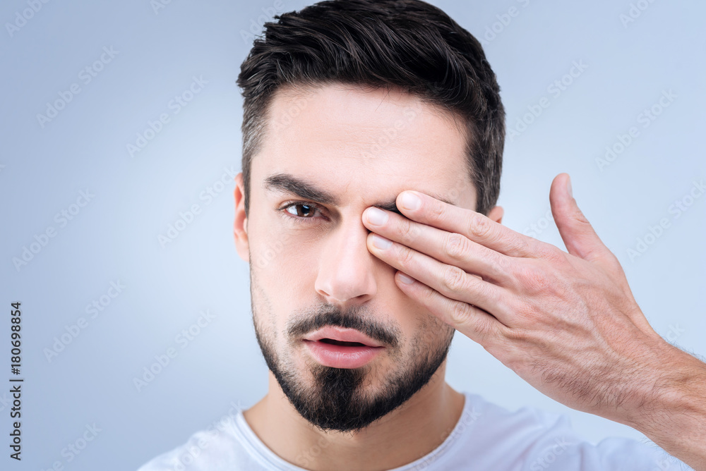 Checking eyesight. Serious responsible handsome man being concentrated while closing his right eye to check his eyesight Checking eyesight. Serious responsible handsome man being concentrated while closing his right eye to check his eyesight