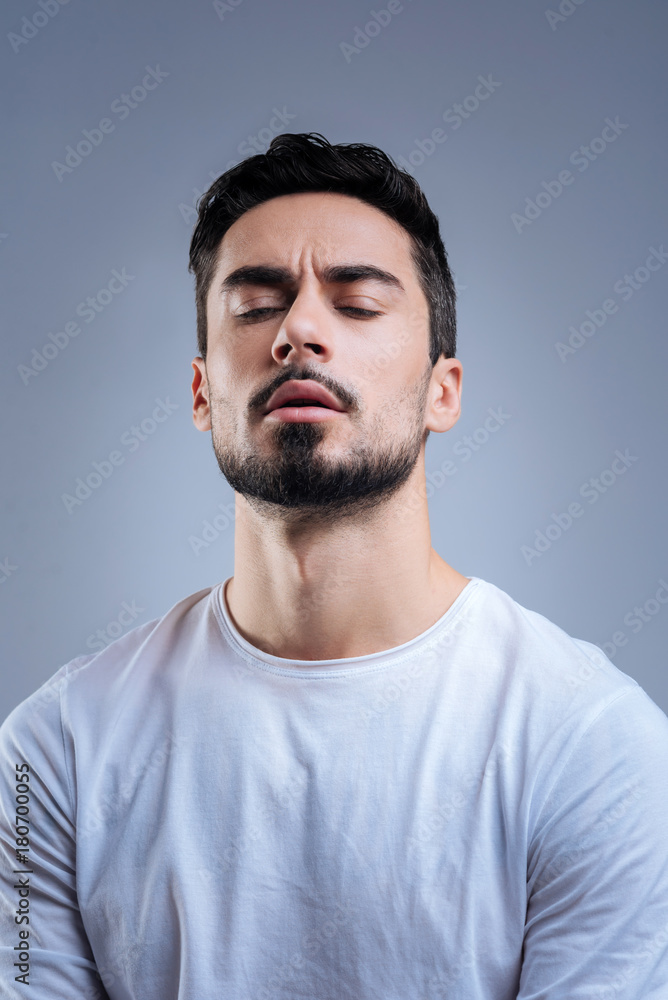 Obraz premium Emotional moment. Expressive young handsome man sitting with his eyes closed and looking impressed while hearing his favorite song