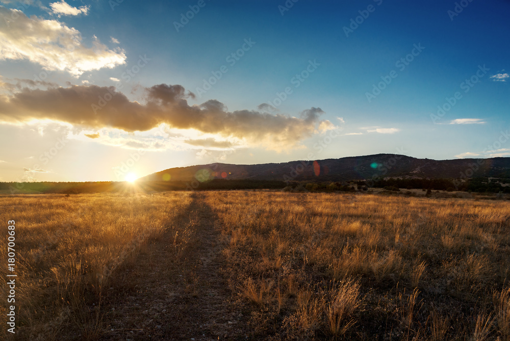 Beautiful orange autumn sunset in dry grass field with road. Mountain background. Beautiful orange autumn sunset in dry grass field with road. Mountain background.