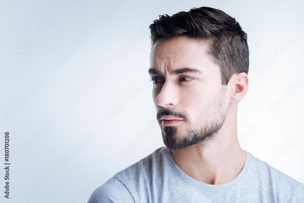 Look away. Calm handsome bearded man looking not pleased with his working day while sitting against the blue background with his head turned right Look away. Calm handsome bearded man looking not pleased with his working day while sitting against the blue background with his head turned right