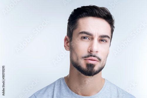 Rather calm. Handsome thoughtful young man feeling calm while sitting against the blue background and slightly frowning